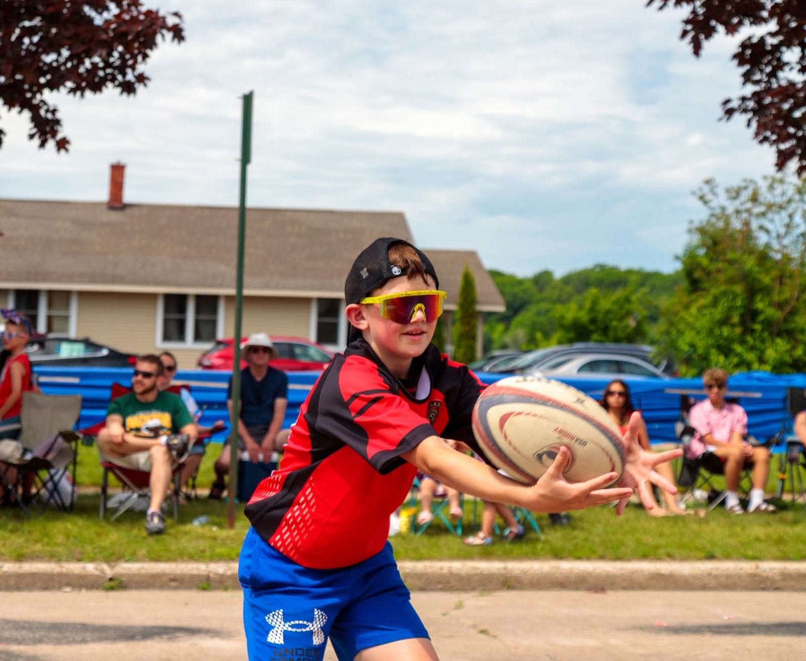 Young Escanaba Berserkers player in a red jersey passing a rugby ball on match day