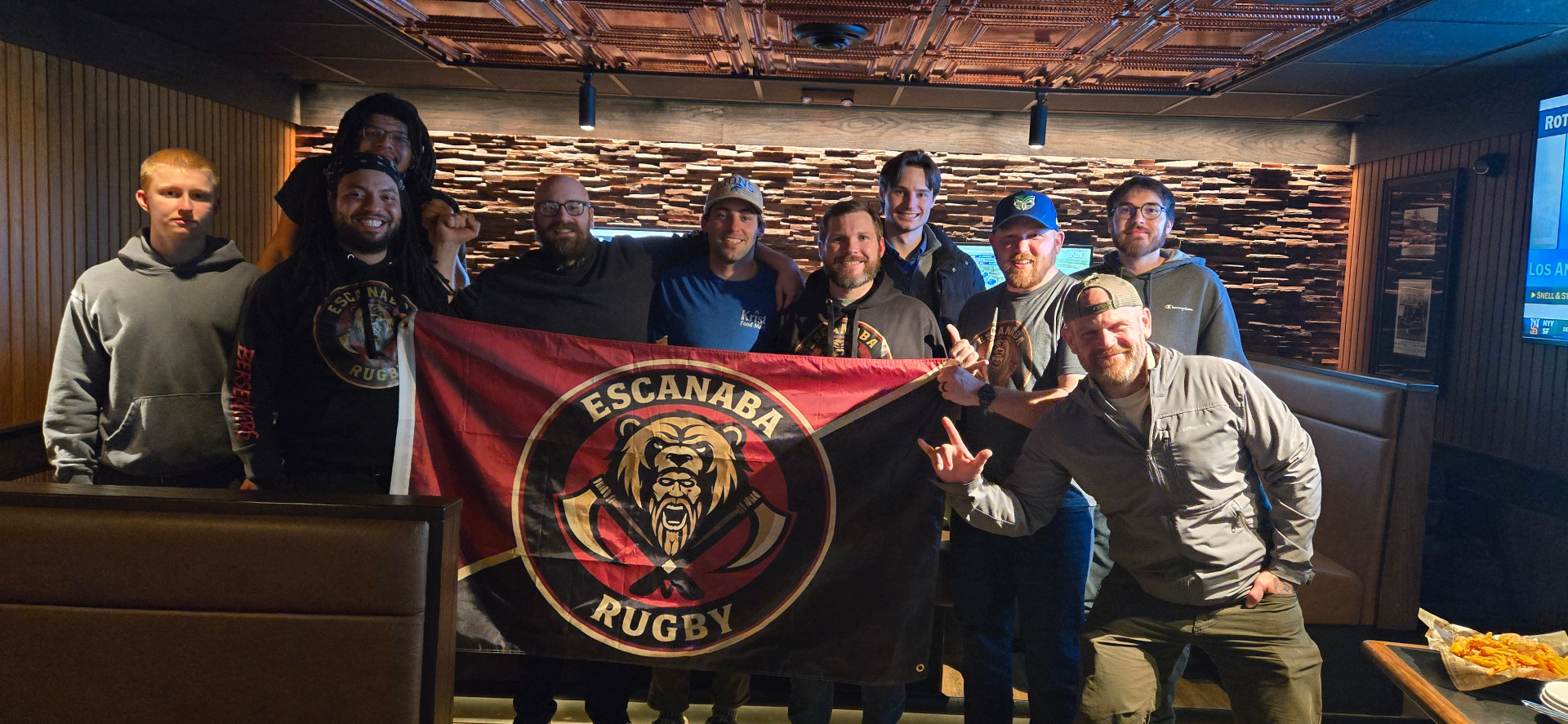 Club members gathered around the Escanaba Rugby flag at a local pub